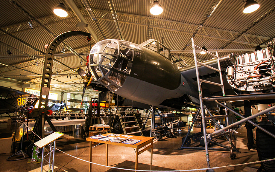 Ett &auml;ldre flygplan under restoration med st&auml;llningar omkring sig. I bakgrunden syns fler flygplan.