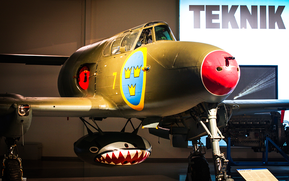 Ett gr&ouml;nt flygplan med r&ouml;d nos och Flygvapnets vapen med tre gula kronor mot bl&aring; bakgrund p&aring; ena sidan.