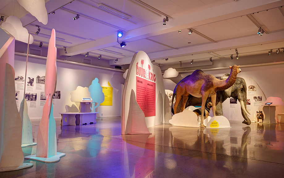 Djur och krig st&aring;r det p&aring; en sk&auml;rm i utst&auml;llningssalen. Framf&ouml;r en elefant- och en kamelstaty. Fler utskurna tr&auml;d i bl&aring;tt och vitt.