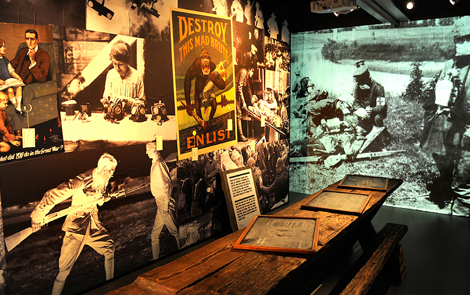 Propagandaaffischer s&aring;som "Destroy this mad brute, enlist" blandas med svartvita fotografier p&aring; m&auml;nniskor i vardagen och soldater i krig.