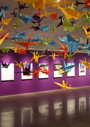 Ett or&auml;kneligt antal f&auml;rgglada origamitranor i papper upph&auml;ngda i taket i en utst&auml;llningssal.