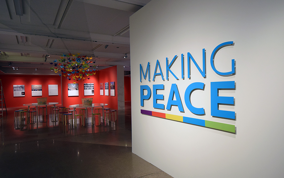 Det st&aring;r "Making Peace" stort &ouml;ver ena v&auml;ggen. I bakgrunden h&auml;nger f&auml;rgglada origamitranor i taket och tavlor tillh&ouml;rande utst&auml;llningen p&aring; v&auml;ggarna.