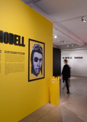 Mot en gul v&auml;gg i en av utst&auml;llningshallarna g&aring;r det att l&auml;sa om &Aring;ke Hodell, l&auml;ngre bort skymtas en bes&ouml;kare.