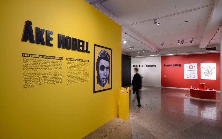 Mot en gul v&auml;gg i en av utst&auml;llningshallarna g&aring;r det att l&auml;sa om &Aring;ke Hodell, l&auml;ngre bort skymtas en bes&ouml;kare.
