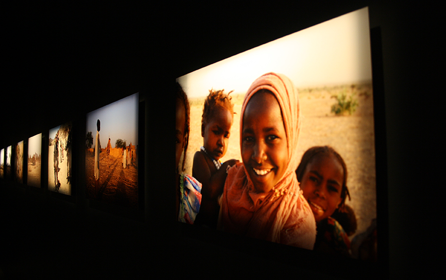 En vuxen med tv&aring; barn ler i bilden som h&auml;nger mot den svarta utst&auml;llningsv&auml;ggen.