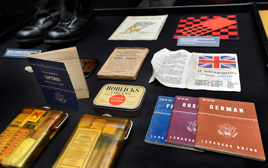 Mot svart bakgrund i en monter st&aring;r ett par svarta skinnskor samt diverse sm&aring; f&ouml;rpackningar och tre spr&aring;kguider f&ouml;r tyska, ryska och franska.