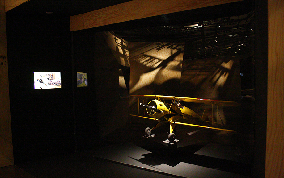 Ett gult modelflygplan av &auml;ldre modell h&auml;nger i en dramatiskt upplyst monter.