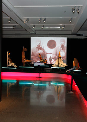 P&aring; ena v&auml;ggen st&aring;r det Katapult i vitt mot svart bakgrund och sedan f&ouml;ljer text om katapultstolens historia. Strax intill st&aring;r flygplansstolar p&aring; rad och visar p&aring; utvecklingen fr&aring;n enklaste tr&auml;stol till de mer avancerade stolar vi k&auml;nner igen i dag.