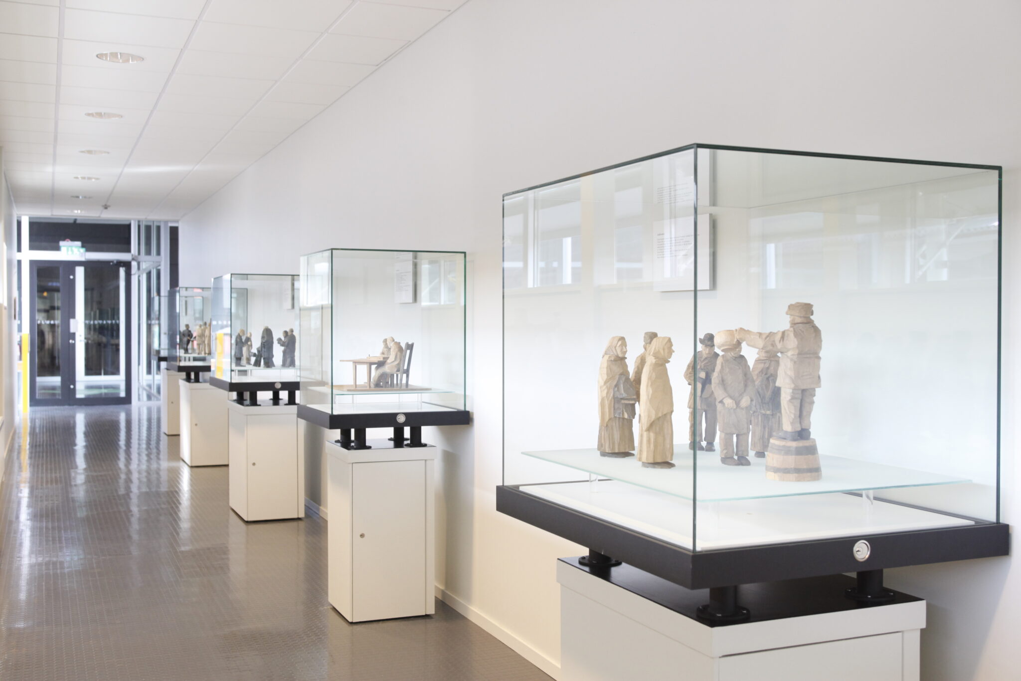 Fem glasmontrar p&aring; rad l&auml;ngs ena v&auml;ggen i en korridor visar upp D&ouml;derhultarns tr&auml;figurer.