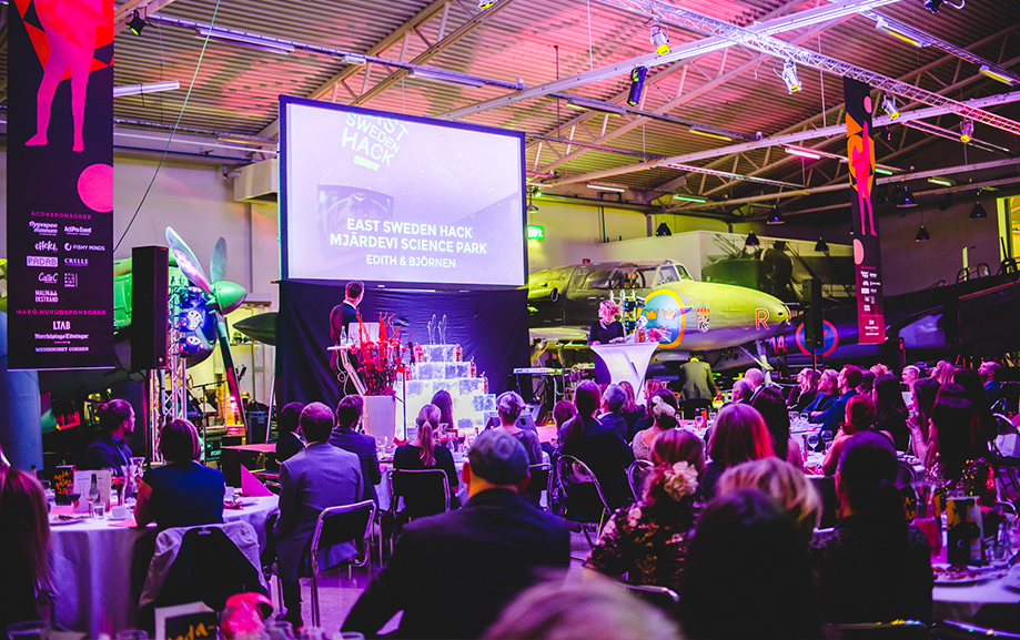 East Sweden hack st&aring;r det p&aring; sk&auml;rmen uppst&auml;lld bland flygplanen i en av utst&auml;llningshallarna. Framf&ouml;r det lilla uppst&auml;llda podiet vid sk&auml;rmen sitter &aring;h&ouml;rare vid uppdukade bord