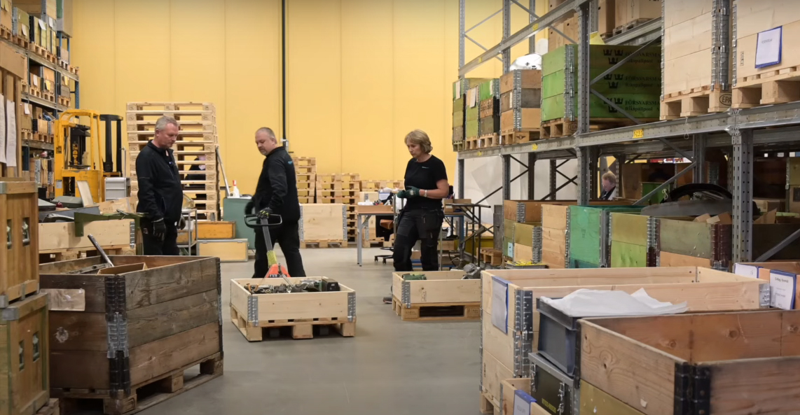 Tre personer i en lagerlokal med l&aring;dor fyllda med saker p&aring; hyllorna runtom.
