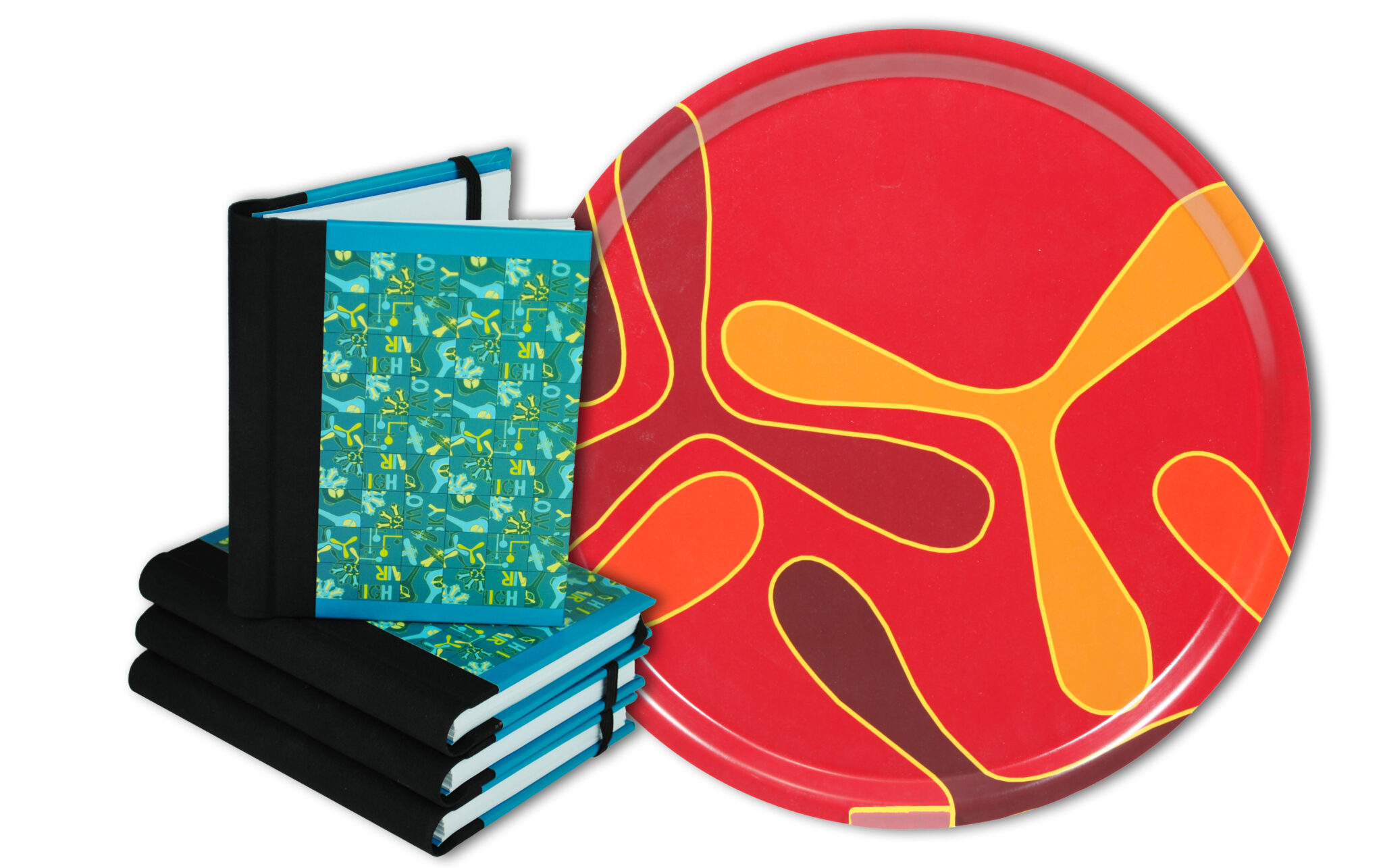 En r&ouml;d bricka med ett abstrakt m&ouml;nster av flygplanspropellrar samt skrivb&ouml;cker med gr&ouml;nbl&aring;m&ouml;nstrat omslag.
