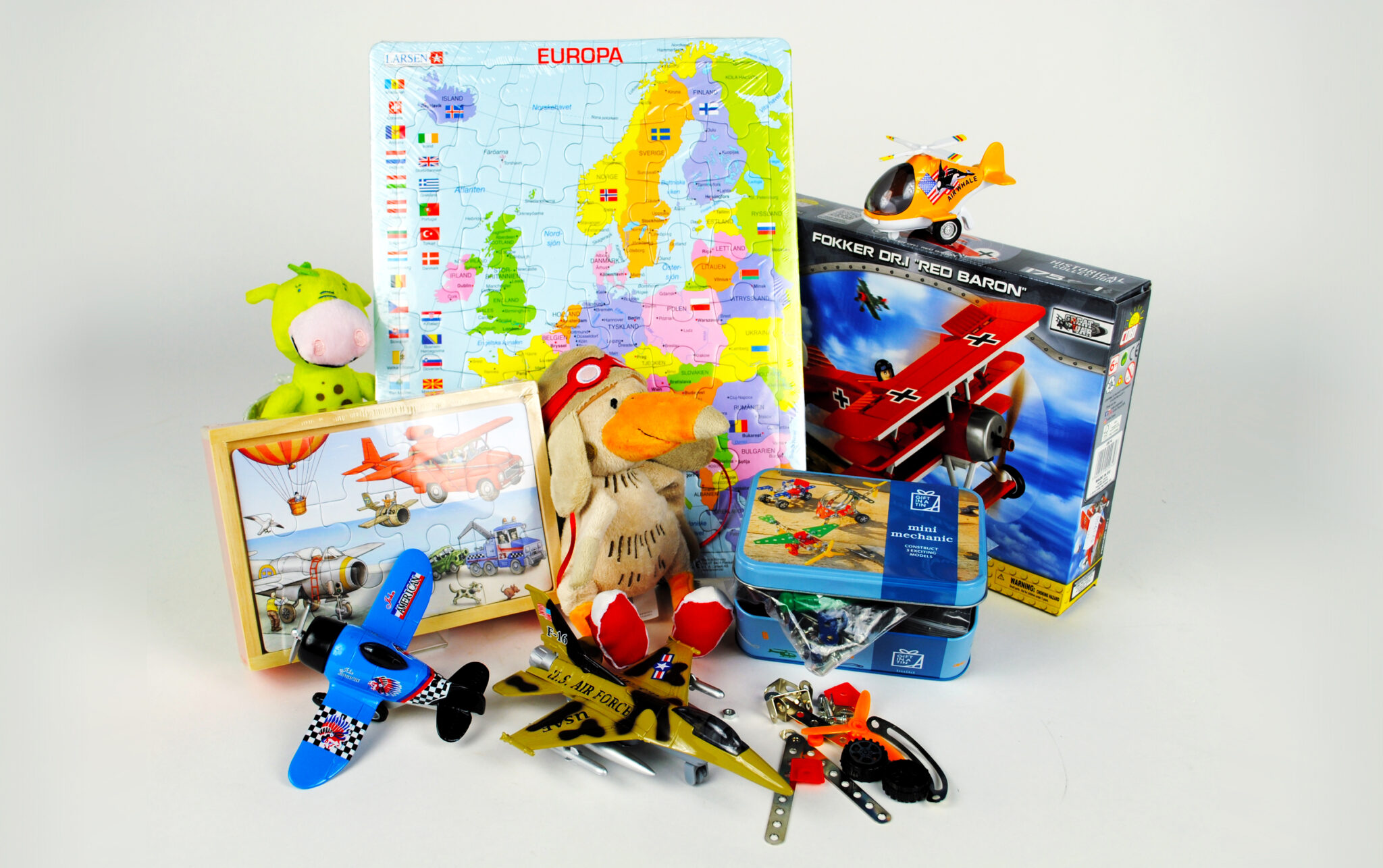 Diverse leksaker st&aring;r uppst&auml;llda mot vid bakgrund, ett pussel &ouml;ver Europa, maskotarna draken Drakel och m&aring;sen Viggo i gosedjursformat, modellsatser f&ouml;r flygplan samt leksakplan och en helikopter redo att leka med.