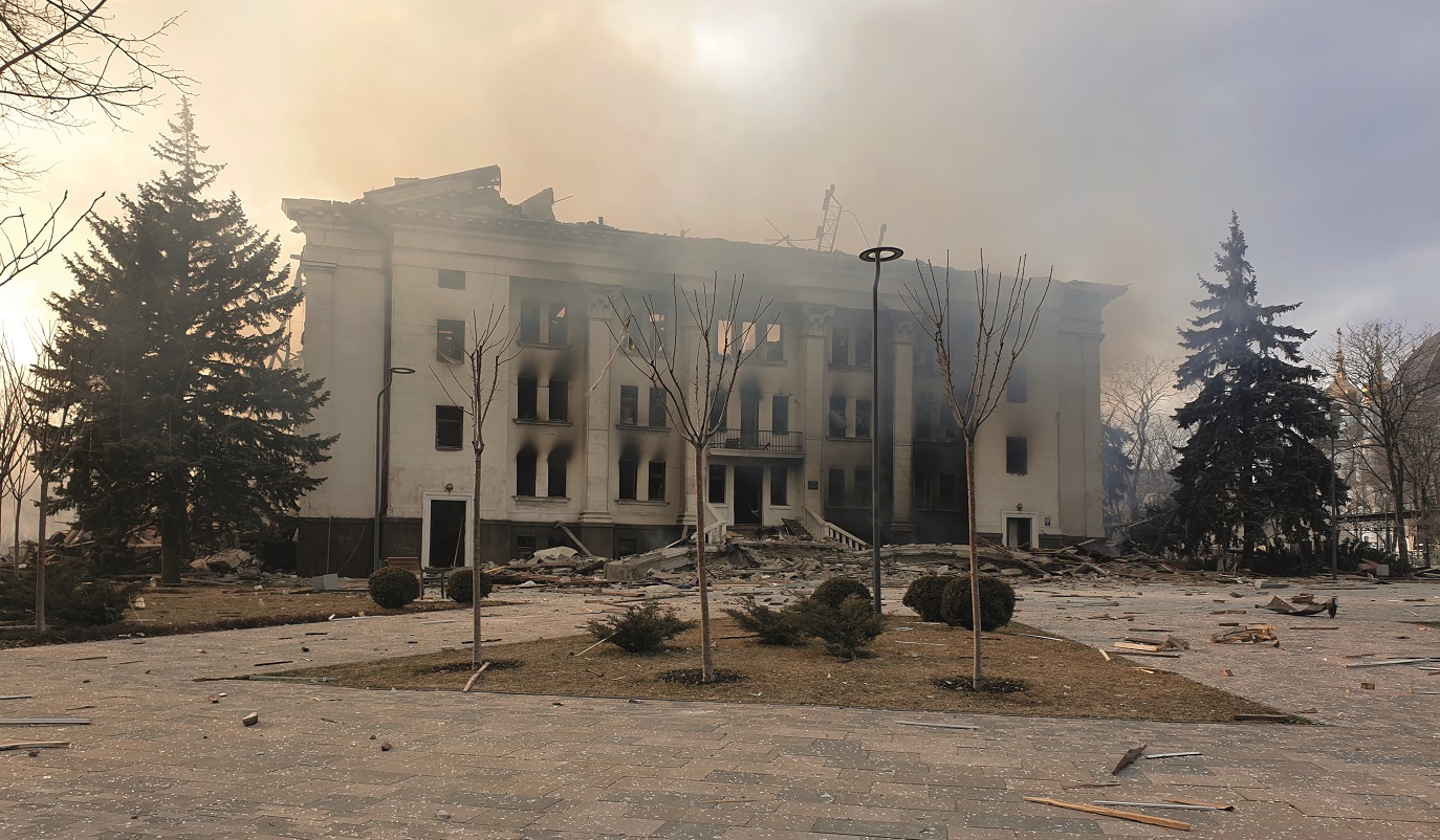 Skelettet av ett vitt stort hus med stenlagd entr&eacute; och granar p&aring; sidorna. Huset ser inte ut att ha n&aring;gra f&ouml;nsterrutor kvar och det verkar ha brunnit.