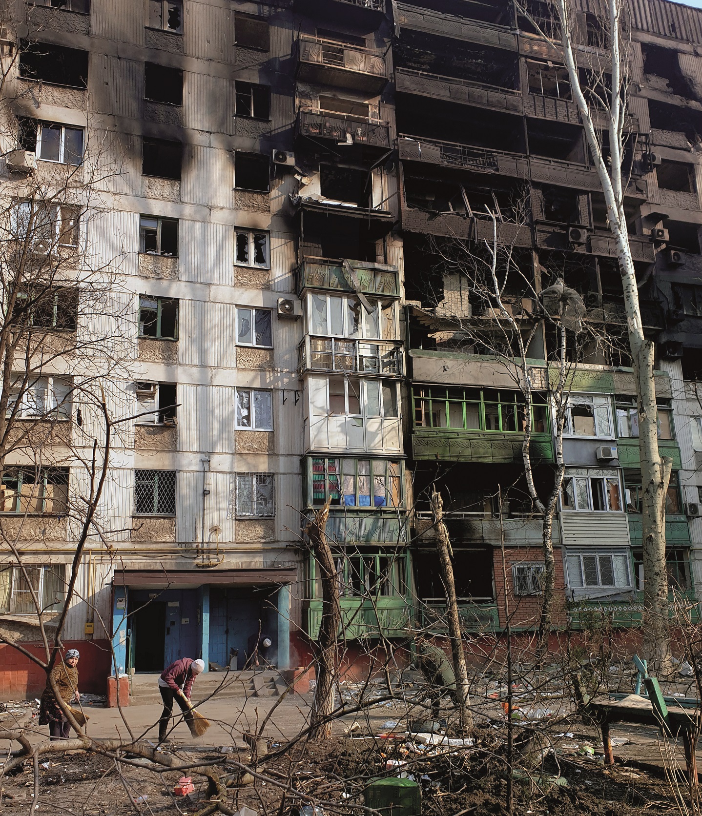 Tv&aring; &auml;ldre personer sopar utanf&ouml;r ing&aring;ngen till ett flerv&aring;ningshus. Flera v&aring;ningar &auml;r svarta efter brand och bara de nedre l&auml;genheterna verkar fortfarande ha f&ouml;nster kvar.