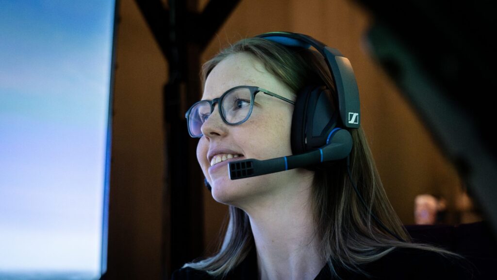 En kvinnlig besökare med långt hår och glasögon ler under flygningen