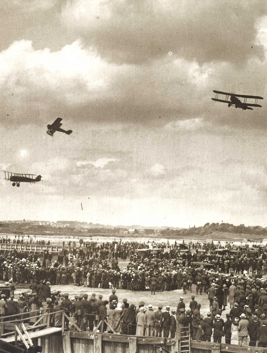 Svartvit bild ur arkivet p&aring; tre flygplan i luften och en folkmassa som st&aring;r nedanf&ouml;r och tittar upp p&aring; dem.